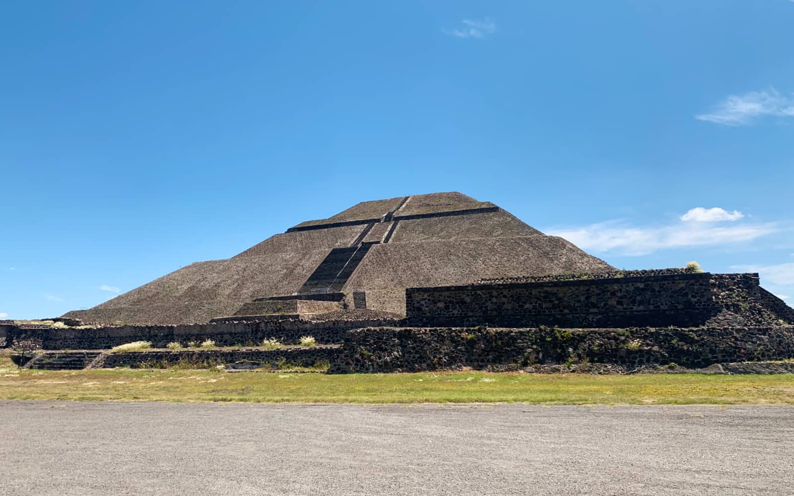 Gravel and grass in the foreground with a massive stone pyramid structure in the background