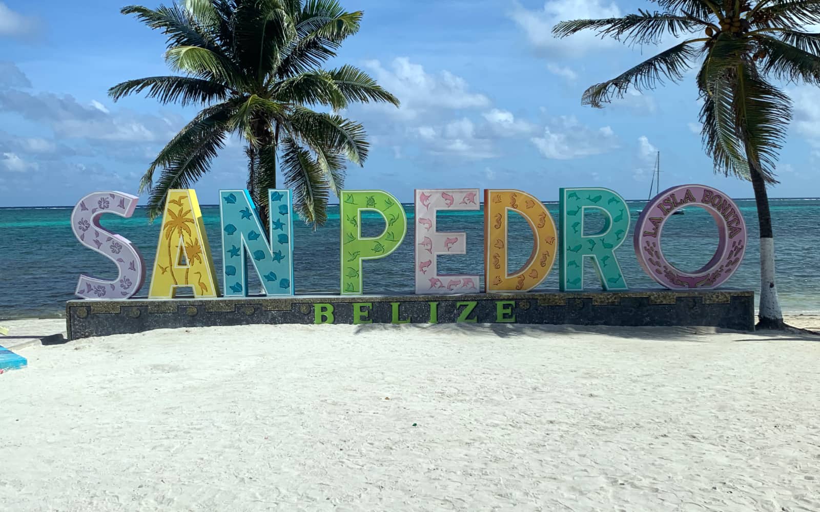 Multi coloured sign spelling out San Pedro, Belize with palm trees and lagoon in background