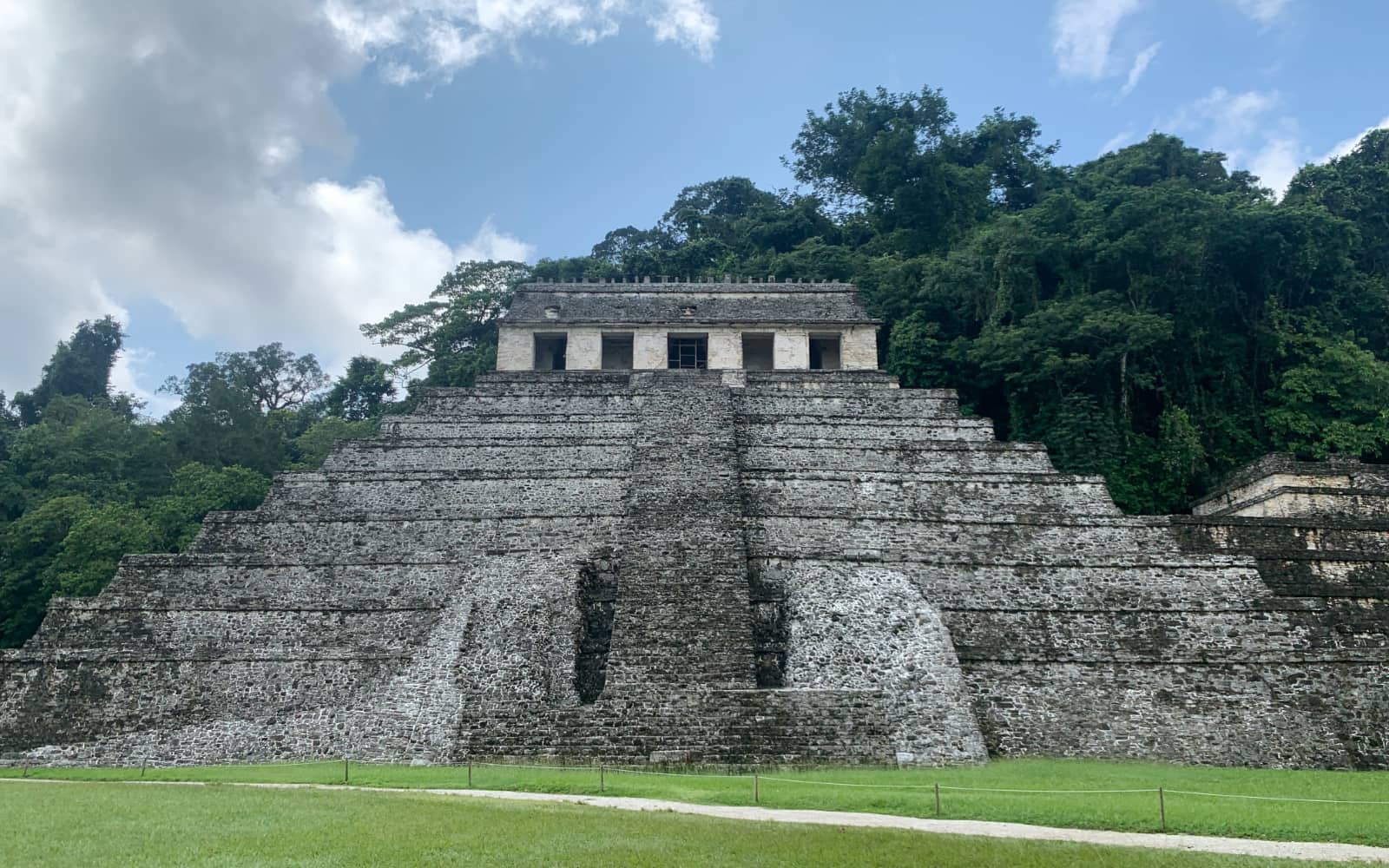 Large stone pyramid structure standing in front lush green trees and blue sky