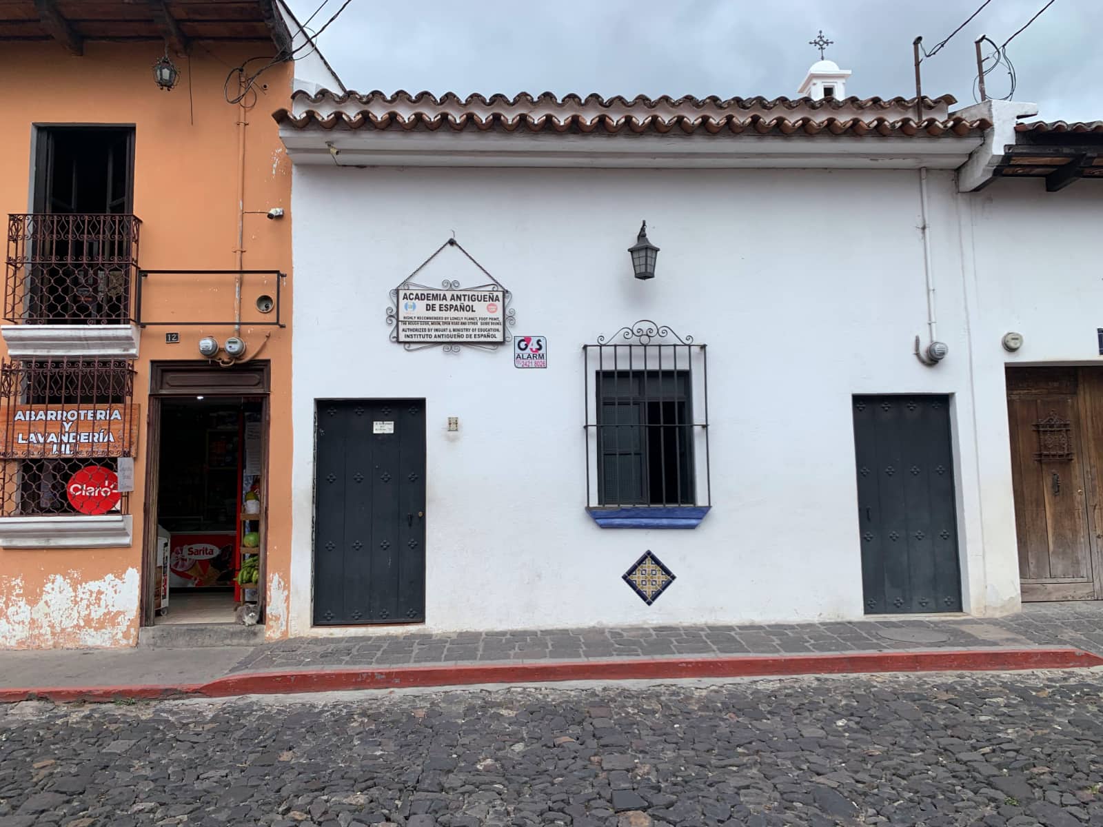 Exteriors of three buildings painted white and peach, with cobble stone roadway in foreground