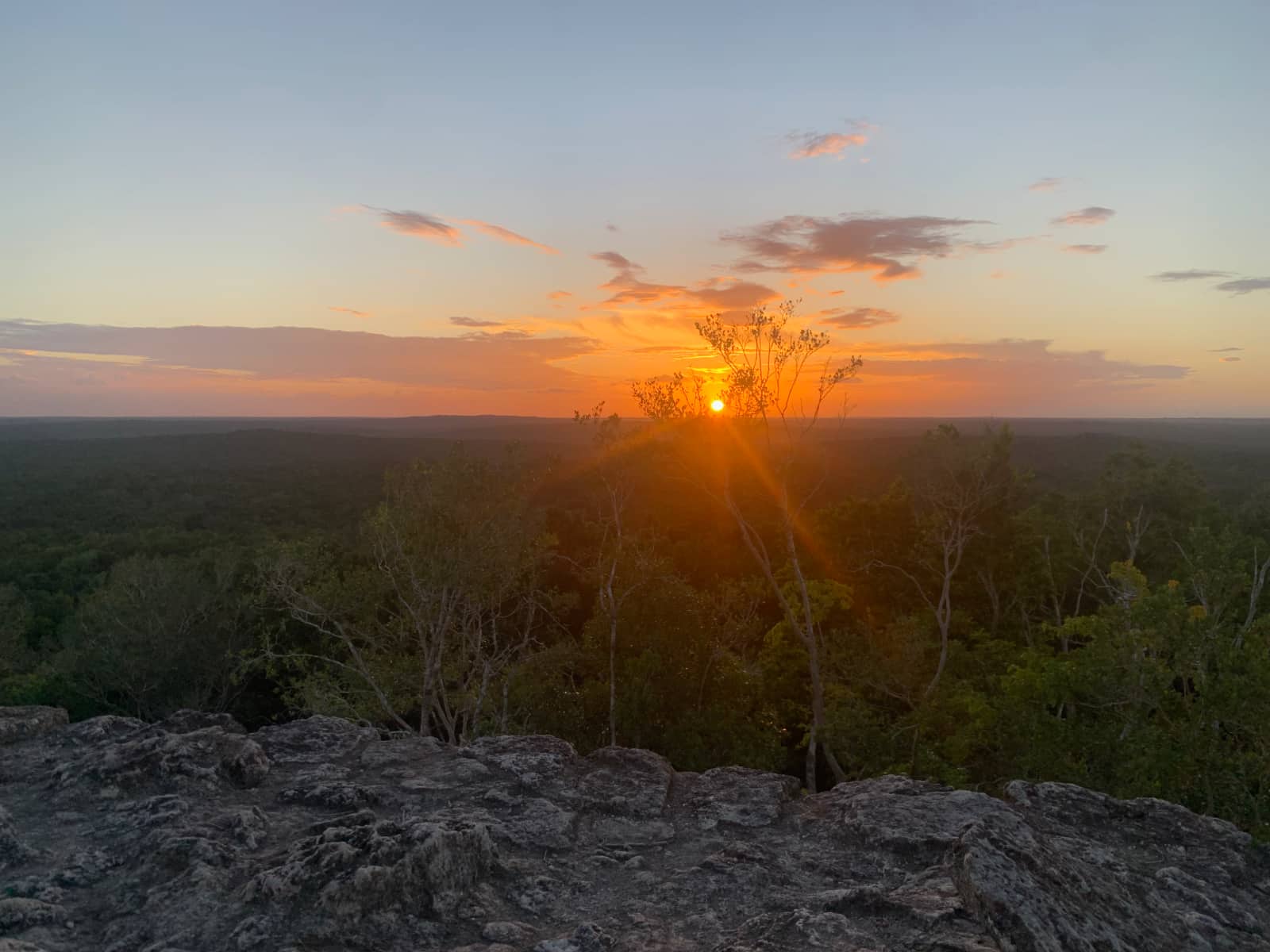 Red orange sun setting over green jungle with a grey stone platform visible in the foreground