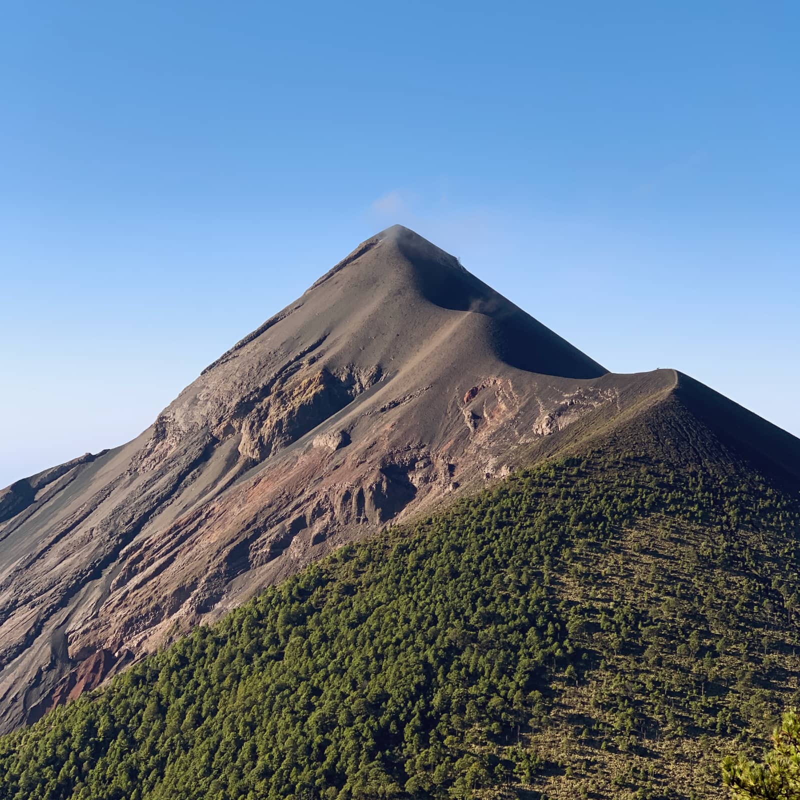 Large, grey volcano in foreground with light blue sky in background