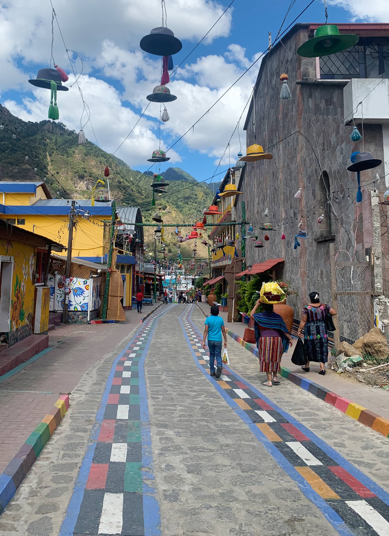 Stone street decorated with colourful road markings, bright yellow painted buildings, and three people walking away in the foreground