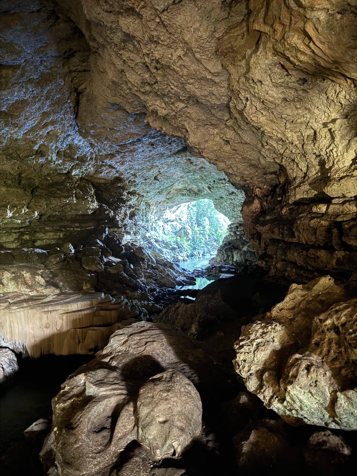 Subterranean cave with beige rock walls in the foreground with sunlight and some water in the background